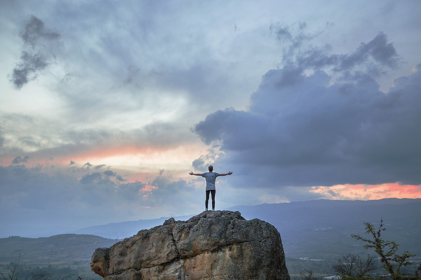 Person steht mit ausgebreiteten Armen auf einem Felsen über den Wolken